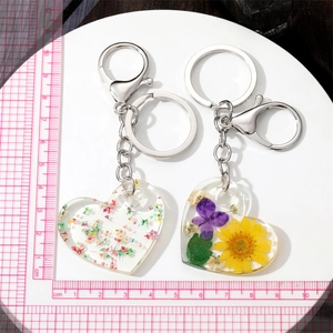 Acrylic heart keychain with real dried flowers and silver lobster clasp on tray