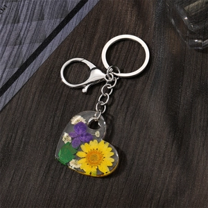 Detail shot of acrylic heart keychain featuring a yellow daisy and real purple dried flowers