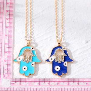 Golden Hamsa hand pendant necklaces with blue enamel and crystal inlay on a white background
