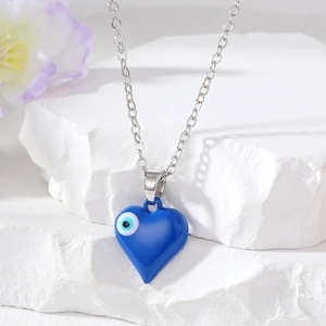 Silberne Halskette mit blauem Herzanhänger und Evil Eye Design auf weißem Steinuntergrund