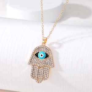 Close-up of a golden Hamsa Hand pendant necklace with clear crystals and an Evil Eye