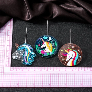 Acrylic unicorn earring set with glittery round charms and metal hooks on fabric