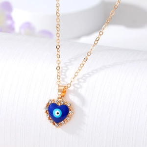 Macro shot of gold heart necklace with blue evil eye enamel and crystal detail