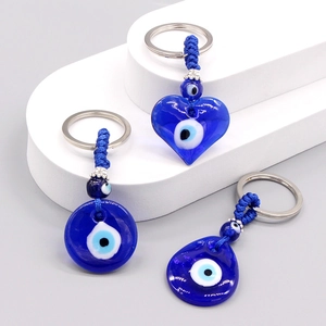 Blue glass Evil Eye keychains in heart and water drop shapes on a white platform