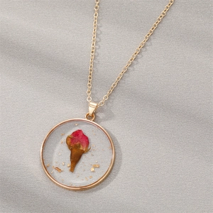 Detail of round resin pendant with real red rose bud and gold foil on grey textile