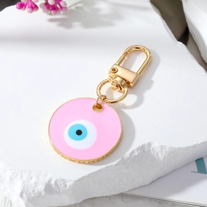 Macro shot of pink enamel evil eye keychain with gold clasp on white stone display
