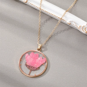 Detailed close-up of a pink dried flower resin pendant with gold flakes on grey fabric