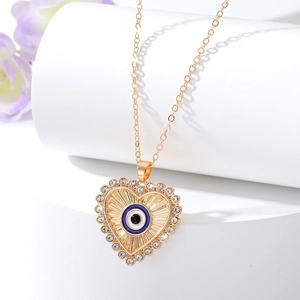 Collana a cuore dorata con ciondolo occhio blu e cristalli su supporto bianco