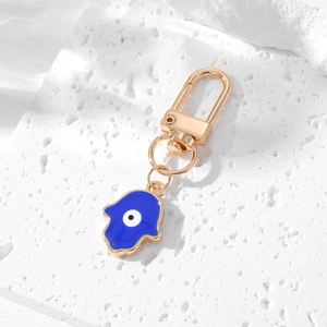 Macro view of golden Hamsa Hand keychain with blue evil eye on white marble background