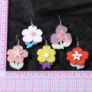 Boucles d'oreilles fleurs en acrylique colorées avec règle de mesure sur fond noir