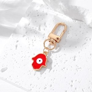 Golden Hamsa Hand keychain with red enamel Evil Eye pendant on stone surface