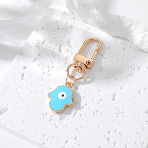 Golden Hamsa hand keychain with blue evil eye enamel on a white stone background