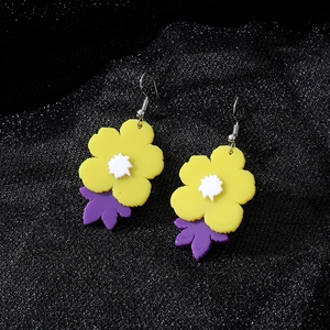 Détail de boucles d'oreilles fleurs en acrylique jaune et feuilles mauves sur tissu noir