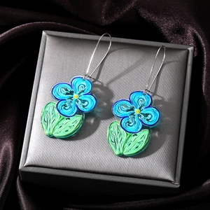 Artistic blue flower drop earrings with green leaves and silver hooks on a jewelry box
