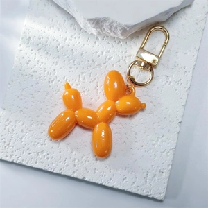 Detail of glossy orange balloon dog keychain with golden metal clasp on stone background