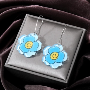 Detailed view of blue acrylic flower earrings with yellow centers on a grey satin box