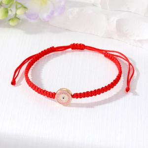 Macro detail of red woven Evil Eye bracelet with pink enamel charm and golden finish