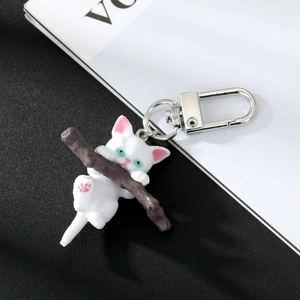 Macro shot of cute white cat hugging a branch keychain with a silver carabiner clip
