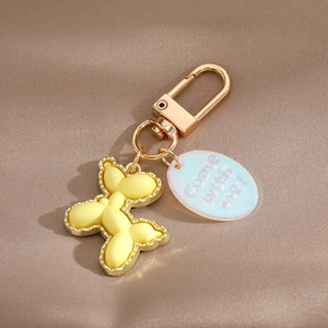 Detail of matte yellow balloon dog keychain with golden alloy edges and oval tag