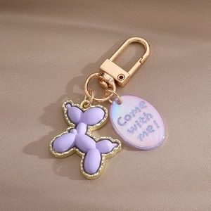 Detail of purple balloon dog keychain with golden metal edges and a charm on fabric