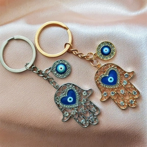 Detailed view of silver and gold Hamsa Hand keychains with blue Evil Eye charms on silk