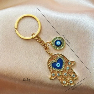 Detail of Hamsa and Evil Eye gold keychain with blue heart enamel on soft pink satin