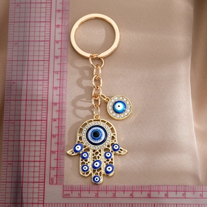 Golden Hamsa Hand Evil Eye keychain with crystals on luxury satin background