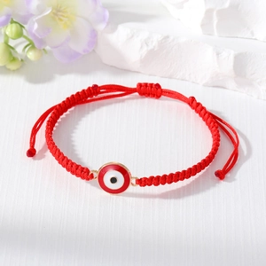 Close-up of handmade red braided cord bracelet with gold-edged evil eye charm detail