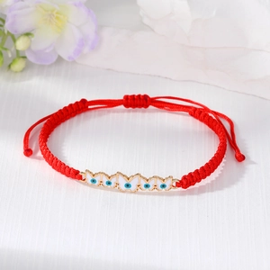 Detail of red woven cord bracelet featuring white butterfly charm and Evil Eye motif