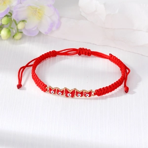Macro detail of red woven bracelet with red enamel butterfly charms and evil eye design