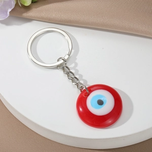 Close-up of a resin evil eye keychain with silver metal chain and ring on a white stand