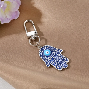 Vintage Hamsa Hand and Evil Eye keychain with blue enamel detail on textured fabric