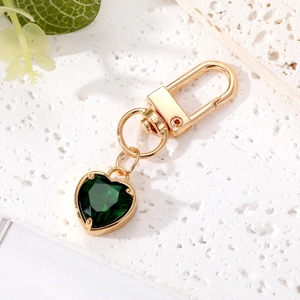 Elegant gold keychain with emerald heart crystal charm on a textured stone surface
