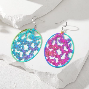 Macro detail of rainbow gradient butterfly hollow earrings on white stone background