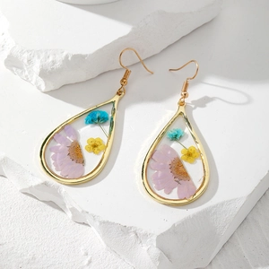 Dettaglio degli orecchini a goccia con margherite viola e fiori secchi in resina