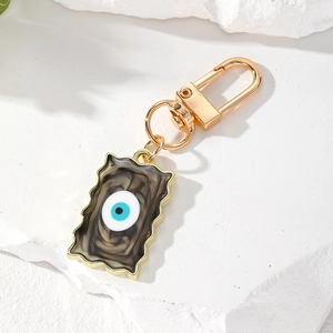 Blue Evil Eye pendant keychain with gold wave frame and smoky resin pattern on stone background