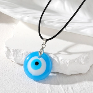 Détail macro du pendentif œil bleu en résine avec cordon noir sur socle en pierre