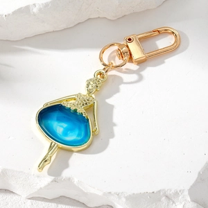 Porte-clés ballerine dorée élégante avec jupe en résine bleue sur fond de pierre blanche