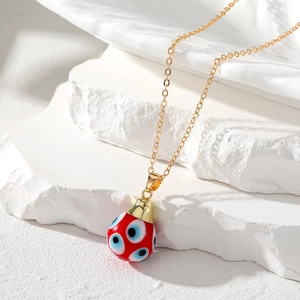 Close-up of red teardrop evil eye pendant with golden chain on white stone