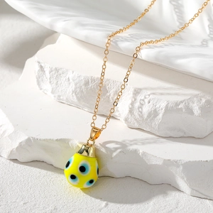 Close-up of a gold chain with a yellow teardrop Evil Eye charm on a stone base