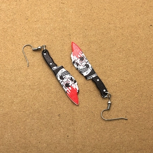 Detail of gothic acrylic hook earrings with skull motif and red blood splatters on knife shape