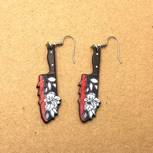 Detail of gothic acrylic earrings featuring bloody chef knife design with white floral patterns