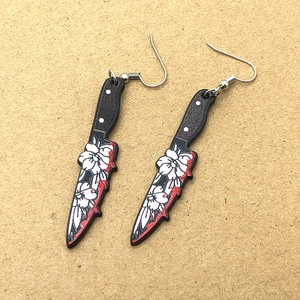 Gothic dagger earrings with floral prints and blood splatter details on brown paper