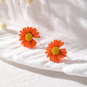 Nahaufnahme von orangen mattierten Gänseblümchen-Ohrringen auf einem weißen Tablett