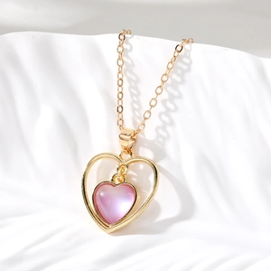 Détail d'un collier cœur doré évidé avec pendentif opale rose sur vagues blanches