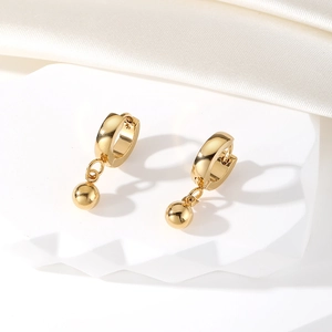 Detailed macro view of golden ball drop hoop earrings on a luxury white fabric background