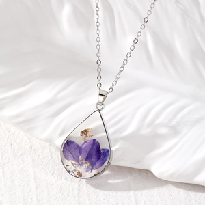 Detail of teardrop glass necklace with purple dried flowers and gold leaf accents
