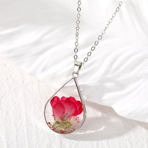 Macro shot of teardrop resin pendant featuring a real red rose flower and gold foil details