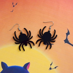 Detailed macro view of black acrylic spider earrings on Halloween moon background