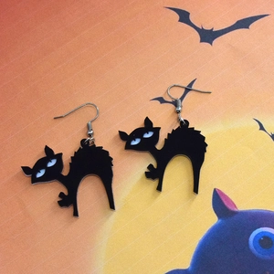 Detail of Halloween black cat acrylic earrings on a spooky orange moon background